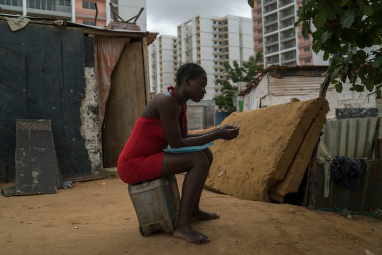 A woman outside her home in the shadow of a large gated housing project away from Luanda (Photo: Joao Silva/The New York Times)